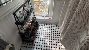 Un bagno con pavimento in piastrelle esagonali bianche e nere, una finestra vista esterna, una tenda da doccia e uno scaffale con articoli da toilette.