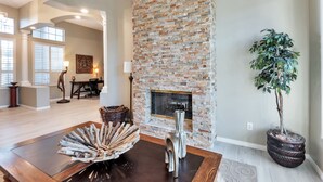 A spacious living room with a brick fireplace, a dining area with a wooden table, and a large potted plant. - FANTASTIC Scottsdale location! Close to Waste Management Open, and Westworld!! (Scottsdale)