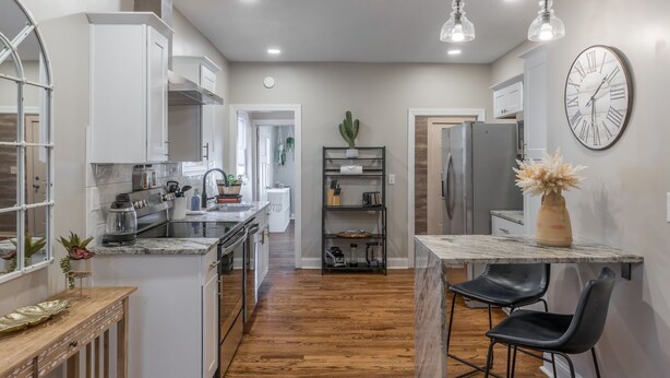 A modern kitchen with white cabinetry, a marble countertop, and a dining area with black chairs. - 3 KING Beds + Walk to River Market + Coffee (Kansas City)