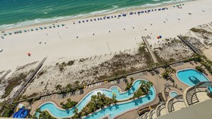 Vista aérea de un resort en la playa con un amplio espacio de piscina, sombrillas y un paseo marítimo.