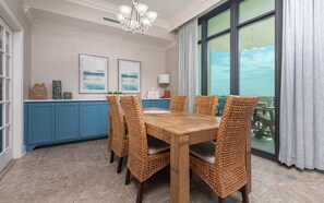 Un comedor con mesa de madera, sillas de mimbre, un armario azul y un ventanal con cortinas.