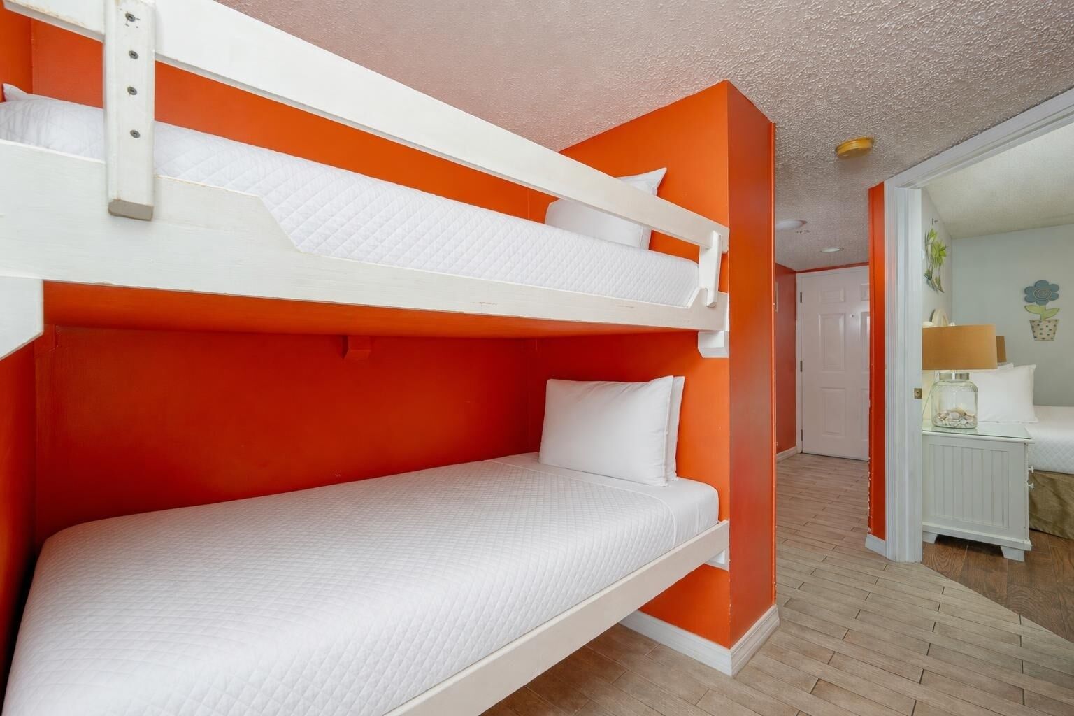 Un lit superposé avec une literie blanche, dans une pièce aux murs orange et au plancher en bois.
