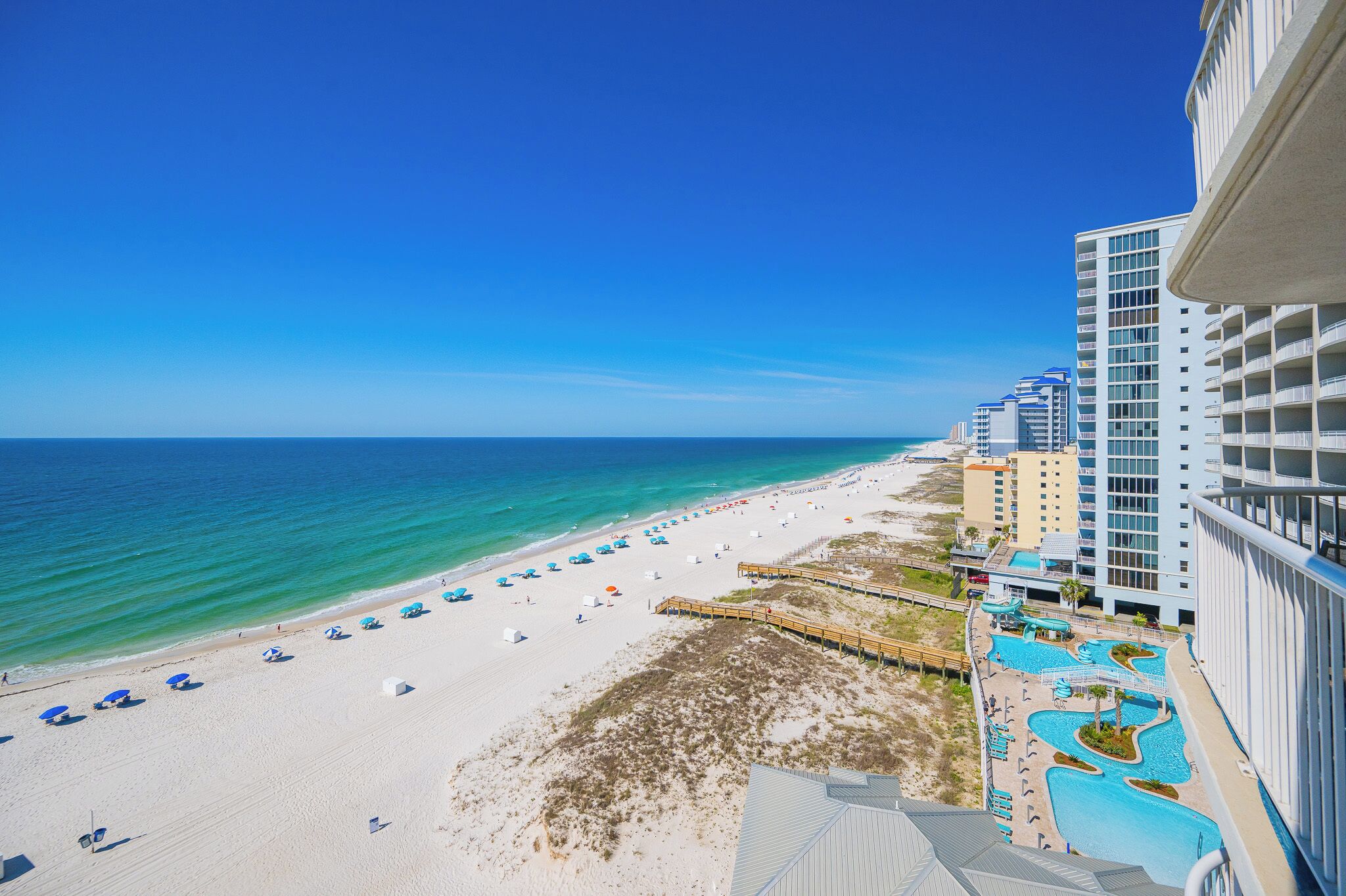 A beach resort with a pool area, beach umbrellas, and a view of the ocean.