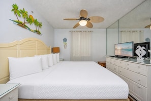 Een hotelkamer met een bed, een televisie, een dressoir, een plafondventilator en een muur met een tropische muurschildering.