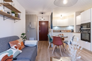 A modern kitchen with white cabinets, a built-in oven, and a dining area with a table and chairs.