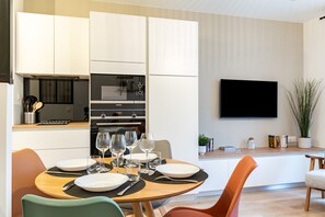 Una cocina moderna con armarios blancos, horno integrado y televisor de pantalla plana montado en la pared.