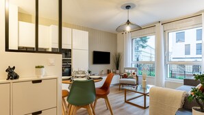 Una cucina moderna con mobili bianchi, una zona pranzo con tavolo e sedie, e un soggiorno con divano e televisore.