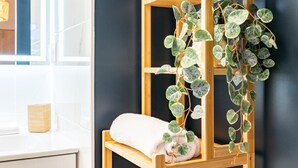 Un bagno con uno scaffale in legno che contiene un asciugamano bianco e una pianta in vaso con foglie variegate.