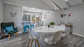 A modern dining area with a round table, white chairs, and a ceiling fan. - Funtierland + Adventure House + Close to Disney + Renovated+ Pool (Anaheim)