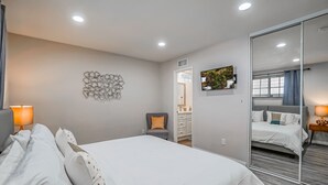 A modern hotel room with a large bed, a mirror, a desk, and a bathroom visible through an open door. - Funtierland + Adventure House + Close to Disney + Renovated+ Pool (Anaheim)