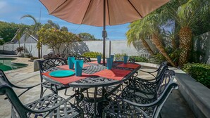 An outdoor patio with a round table, chairs, and a large umbrella. - Funtierland + Adventure House + Close to Disney + Renovated+ Pool (Anaheim)