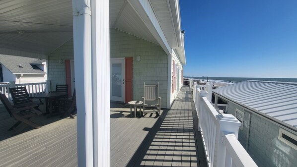 A covered outdoor deck with a table and chairs, a wooden floor, and a view of the ocean.