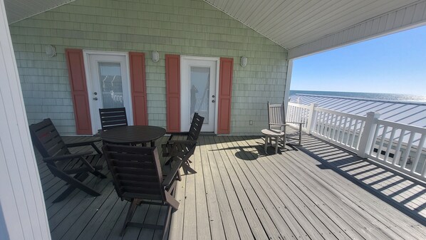 A covered deck with a table and chairs, a white railing, and a view of the ocean.