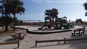 Une aire de jeux sablonneuse avec un toboggan, une table de pique-nique et des bancs.