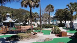 Un parcours de mini-golf agrémenté d’un kiosque, de palmiers et d’un petit étang.