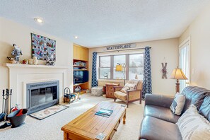 Cozy living room with a fireplace, comfortable seating, and a television, offering a view of the outside through the window.