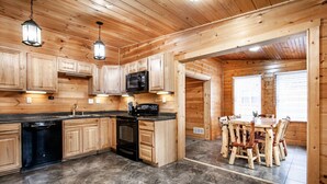 Interior de una cabaña de madera con cocina y comedor, que incluye armarios empotrados, un microondas y una mesa de comedor con sillas.