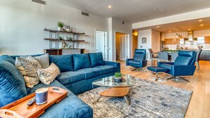 A modern living room with a blue sofa, a glass coffee table, and a wooden tray.