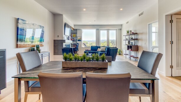 A modern dining area with a marble table and chairs, a kitchen in the background, and a view of the outdoors.