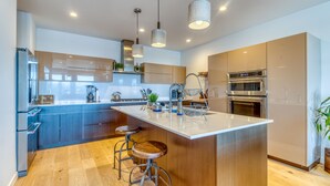 A modern kitchen with a central island, bar stools, stainless steel appliances, and pendant lighting.