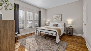 A bedroom with a bed, bedside tables, a window with curtains, a rug, and a plant. - Near downtown Cary & RDU. Easy access to Raleigh, Durham and local venues. (Cary)