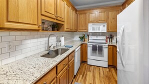 A kitchen with wooden cabinets, a granite countertop, a white refrigerator, a microwave, an oven, and a sink. - Near downtown Cary & RDU. Easy access to Raleigh, Durham and local venues. (Cary)