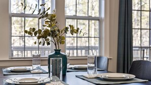 A dining table set with plates, glasses, and a vase with a plant. - Near downtown Cary & RDU. Easy access to Raleigh, Durham and local venues. (Cary)