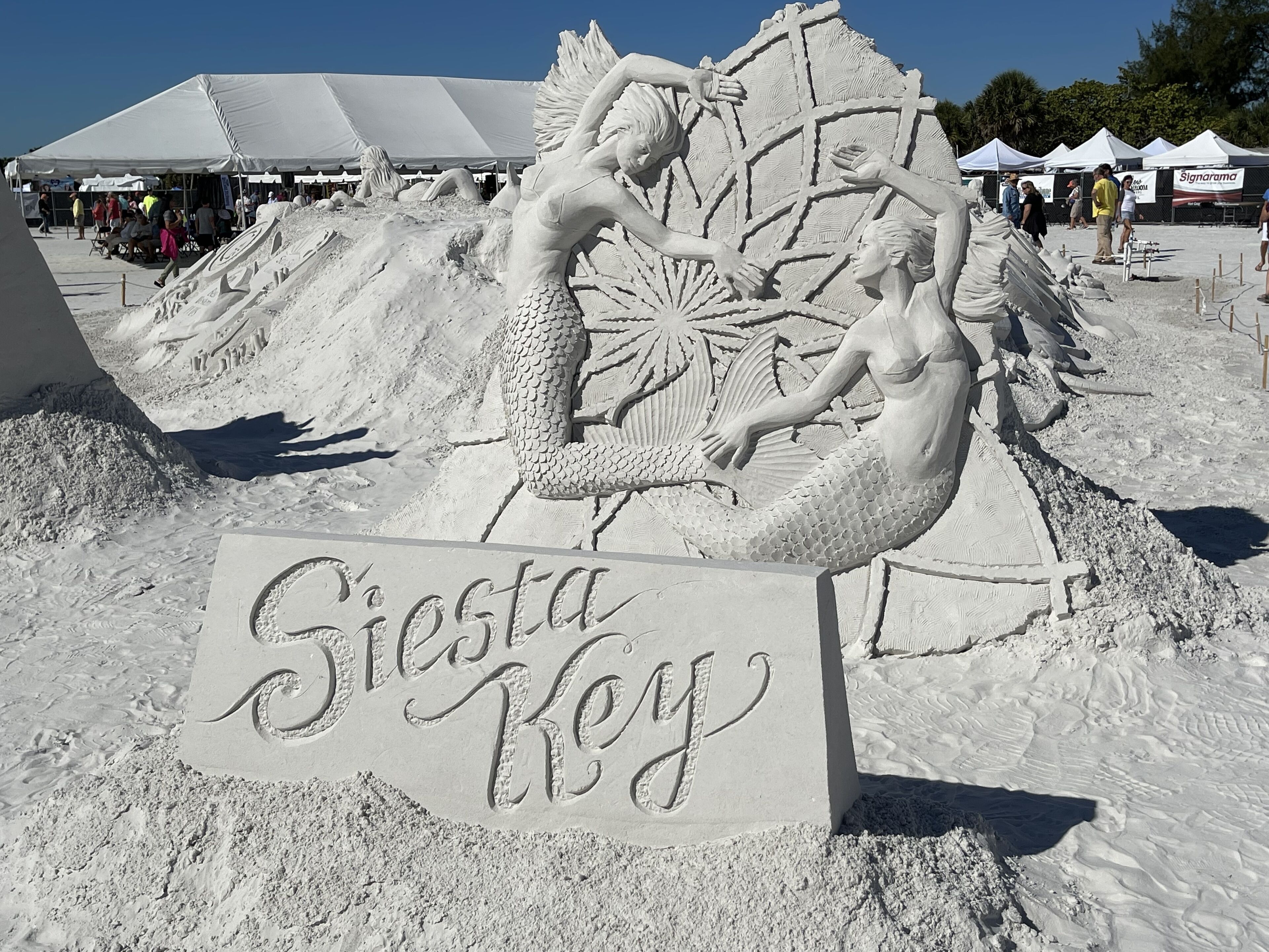A sand sculpture of mermaids with a sign reading "Siesta Key".