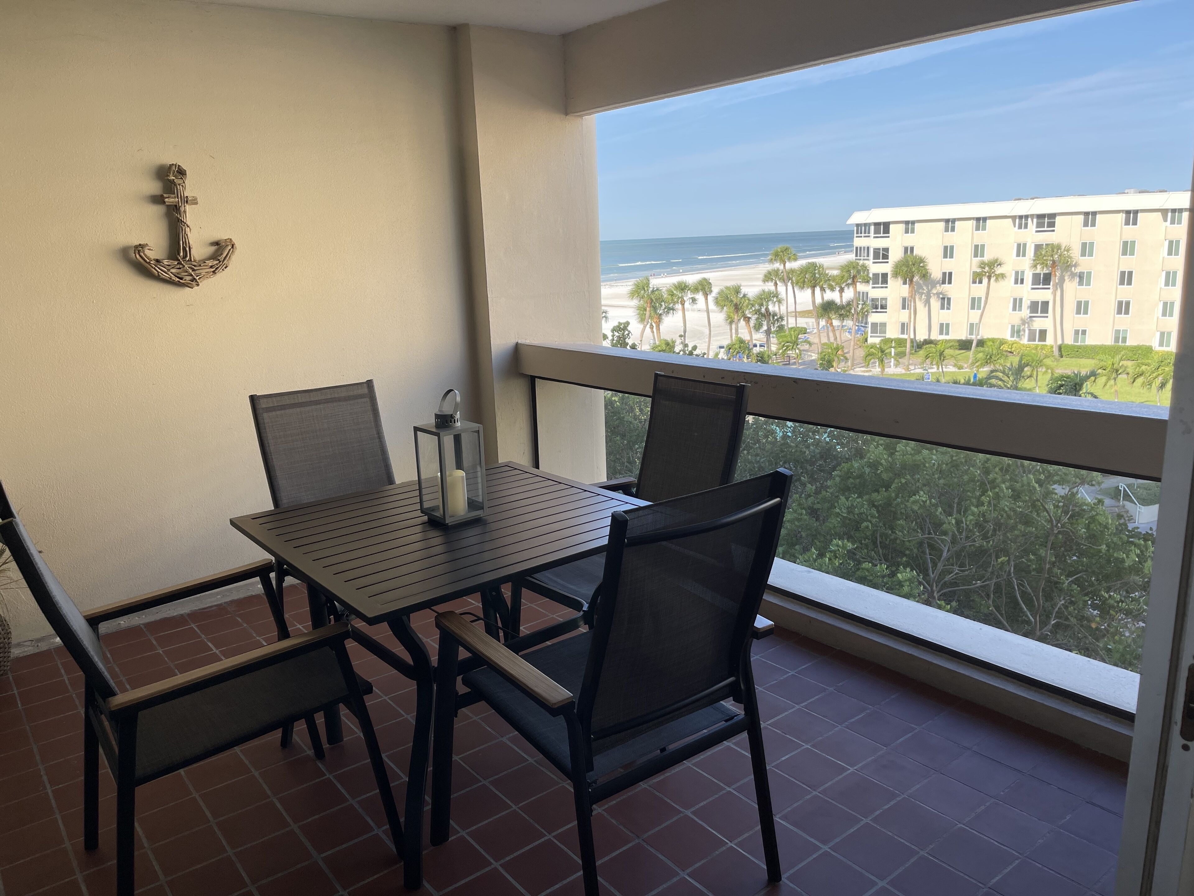 Un balcon avec une table et des chaises, une lanterne, et une vue sur la plage et les palmiers.