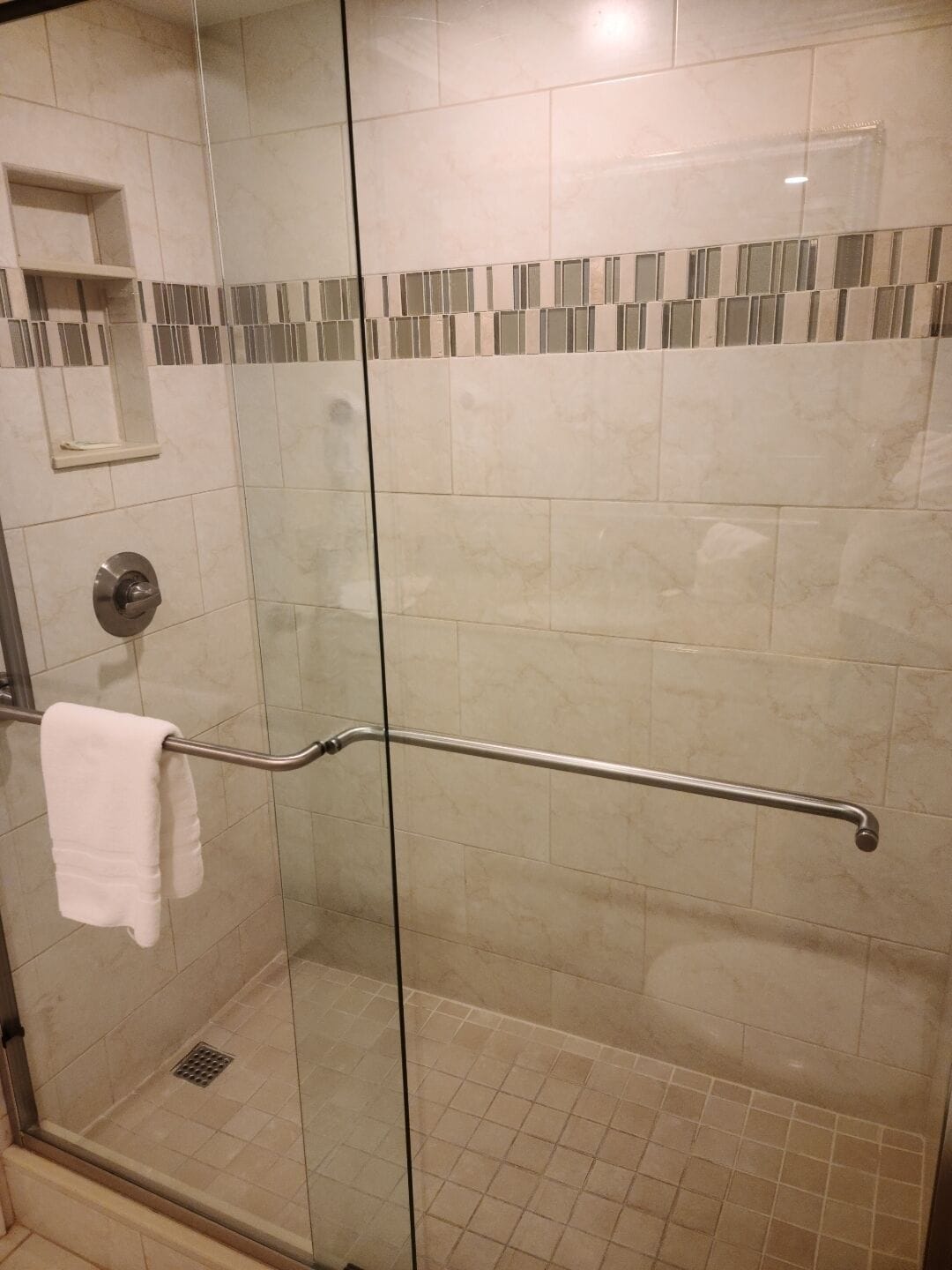 A glass-enclosed shower with a grab bar, a towel rack, and a small shelf.