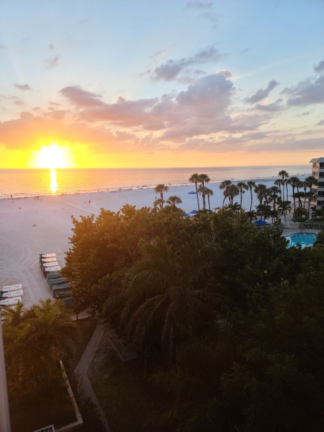 A resort with a pool, palm trees, and a view of the beach at sunset.