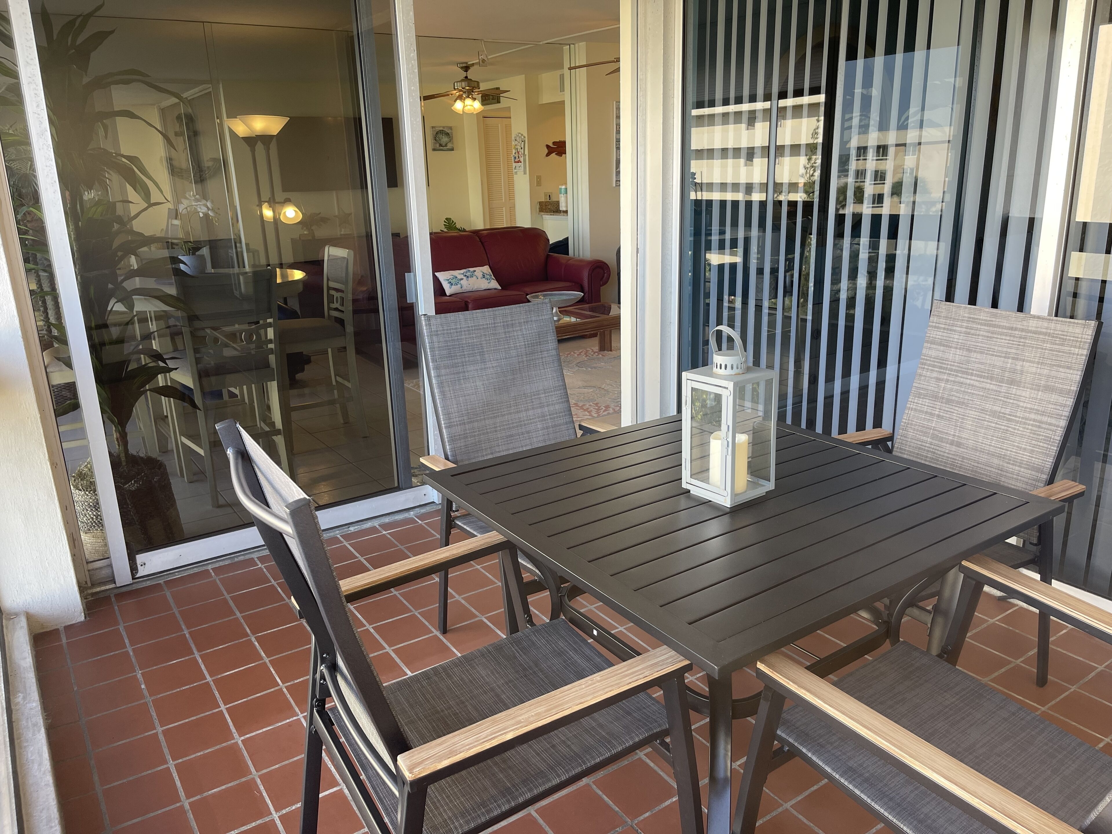 An outdoor patio with a table and chairs, a lantern, and a view of the interior through a glass door.