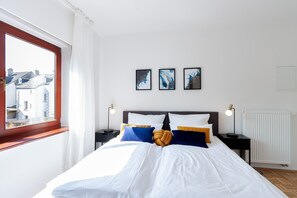 Una camera da letto con un letto grande, due comodini, una finestra con tende e tre quadri appesi al muro.