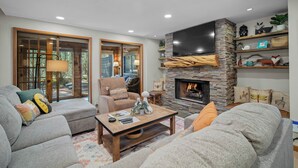 A cozy living room with a stone fireplace, comfortable seating, and a flat-screen TV mounted above it.