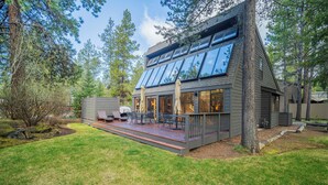 A modern house with a deck, large windows, and a well-maintained lawn.