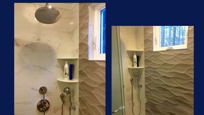 Een badkamer met een marmeren wand, een douche met regendouche en een raam met uitzicht op bomen.