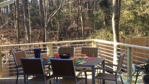 Een houten terras met een tafel en stoelen, omringd door een houten hek en bomen.