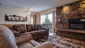 A living room with a stone fireplace, a leather sofa, and a ceiling fan.