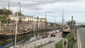 A harbor with boats docked, a stone wall, and buildings in the background. - Riverside@the West Dry (St Austell)