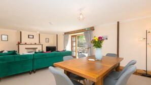 A modern living room with a green sofa, a wooden dining table, and grey chairs. - Riverside@the West Dry (St Austell)