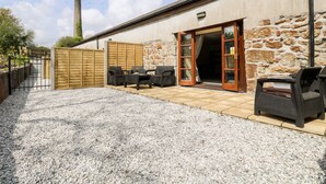 A patio area with outdoor furniture, a stone wall, and a wooden fence. - Riverside@the West Dry (St Austell)
