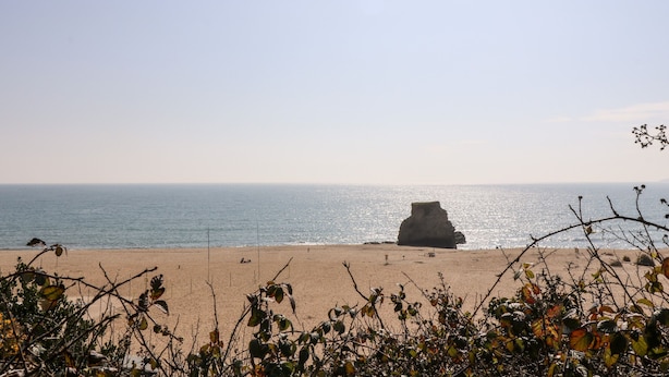A beach with a large rock formation in the distance, clear skies, and calm sea. - Riverside@the West Dry (St Austell)