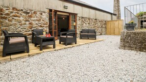 A stone building with a wooden door, outdoor seating with wicker furniture, and a gravel patio. - Water Wheels@the West Dry (St Austell)