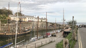 A harbor with boats docked, a stone wall, and buildings along the waterfront. - Water Wheels@the West Dry (St Austell)