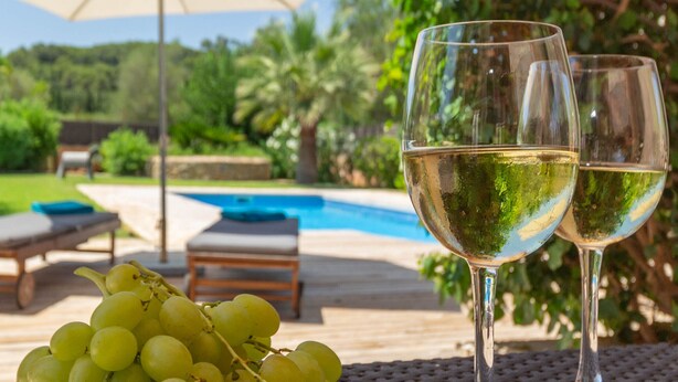 A poolside setting with two wine glasses and a bunch of grapes on a table. - Vista Verde by Balearic Villas (Pollensa)