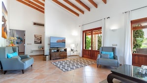A spacious living room with two armchairs, a television, and a large window. - Vista Verde by Balearic Villas (Pollensa)