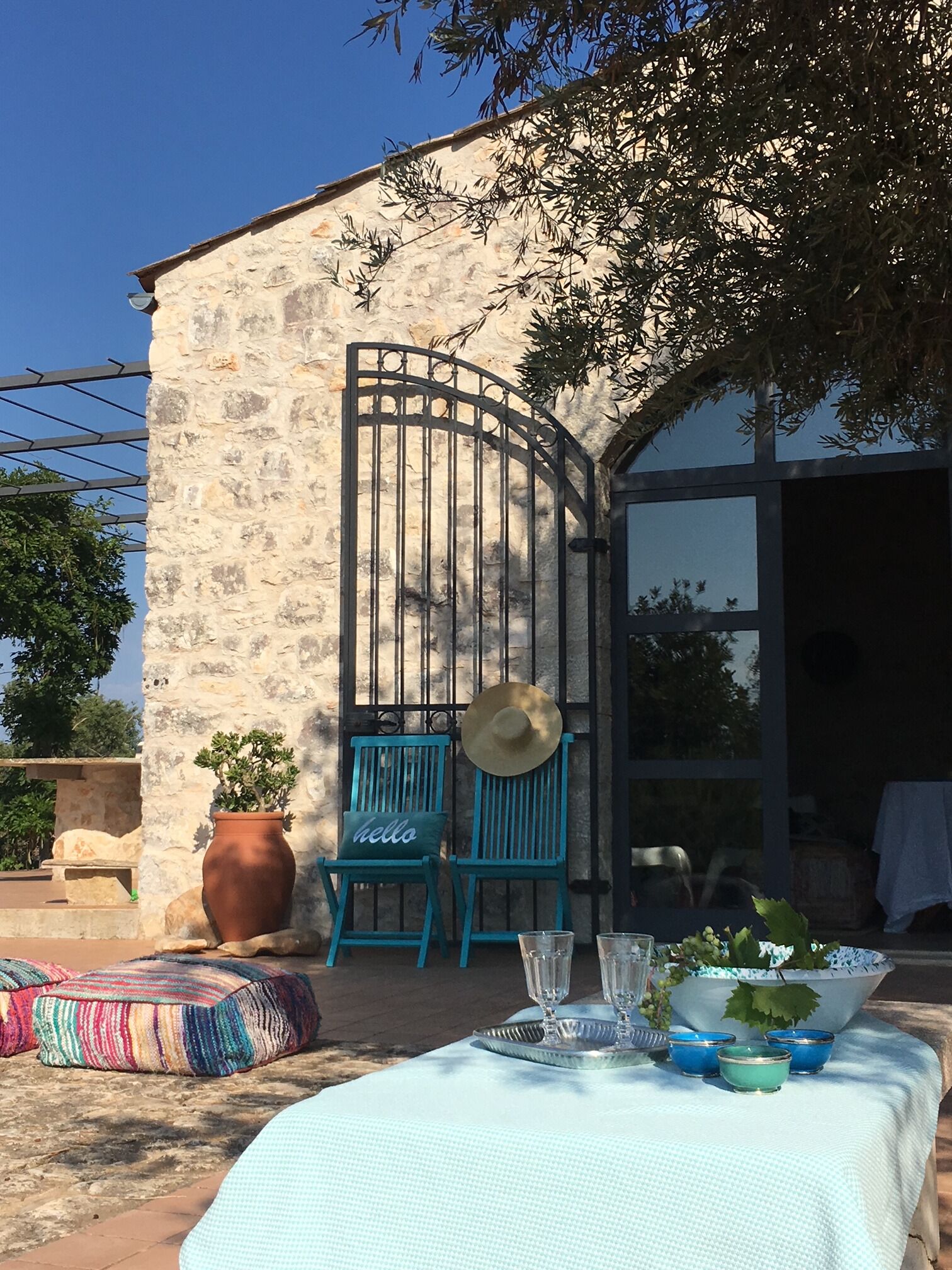 An outdoor seating area with a table set for two, a stone wall, and a metal gate.