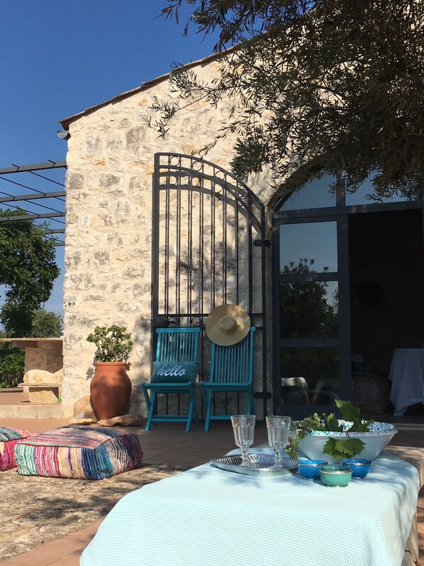 An outdoor seating area with a table set for two, a stone wall, and a metal gate.