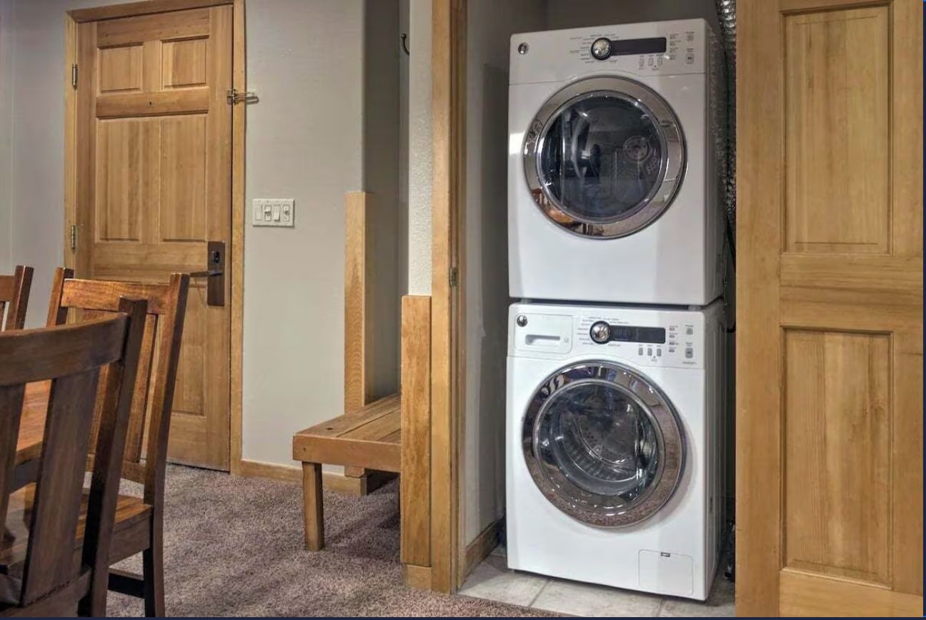 Une buanderie équipée de deux machines à laver à chargement frontal superposées, de portes en bois et d’un petit tabouret en bois.
