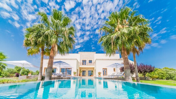 Eine moderne Villa mit Swimmingpool, Palmen und blauem Himmel.
